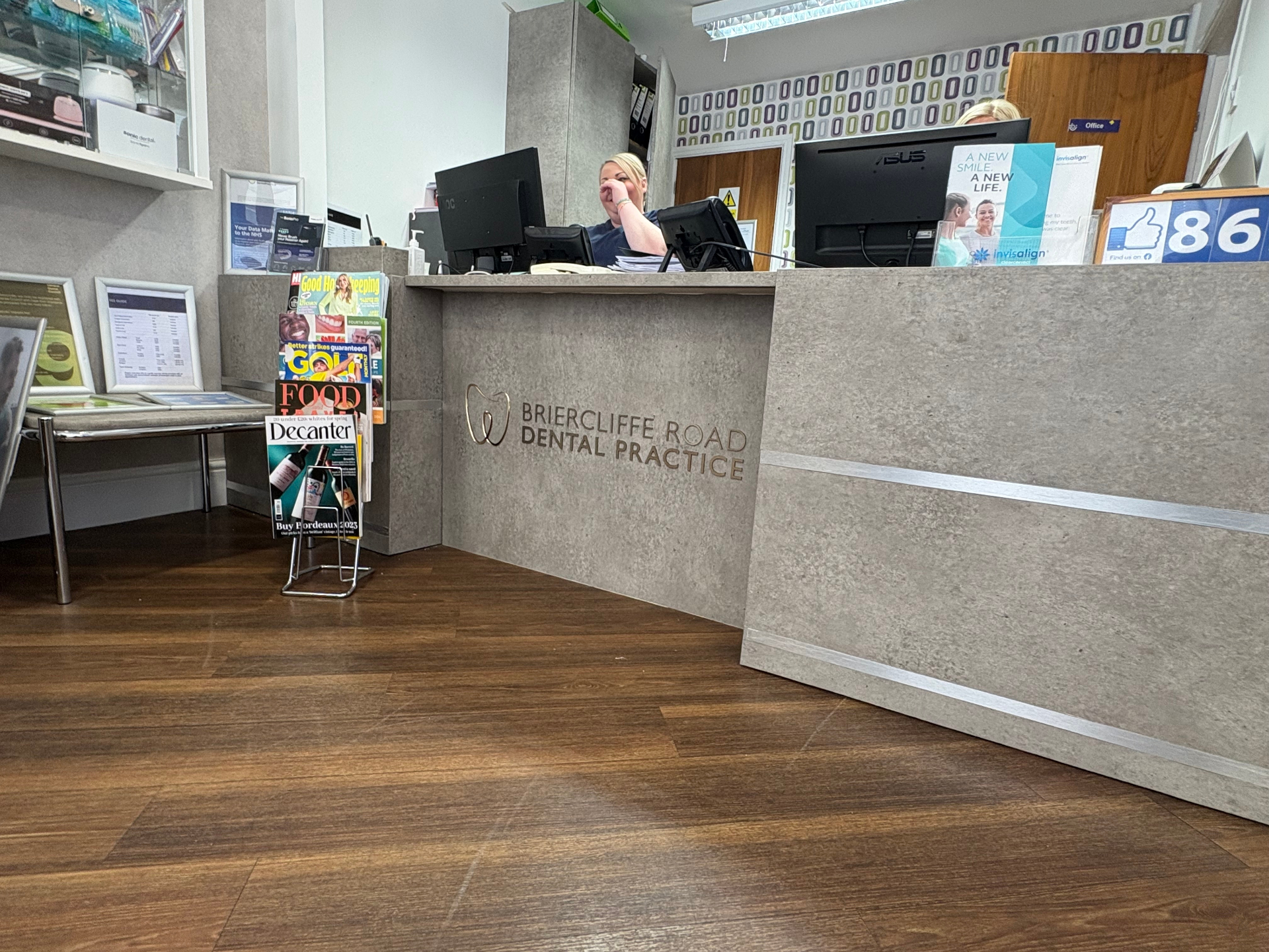 Concrete-effect reception desk wrap with cut brushed brass Briercliffe Road Dental Practice lettering