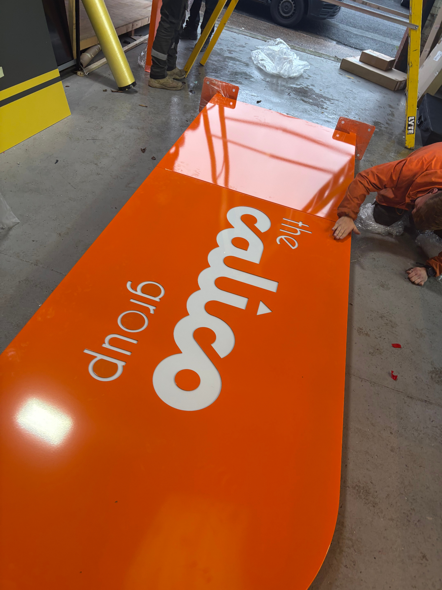 Powder-coated orange Calico Group totem face with cut-out white logo before installation